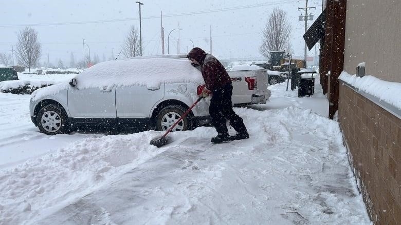A man is pictured shovelling heavy snow in a parking lot. 