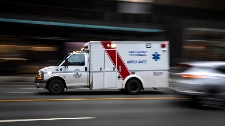 An ambulance runs on the road, with a car running beside it.