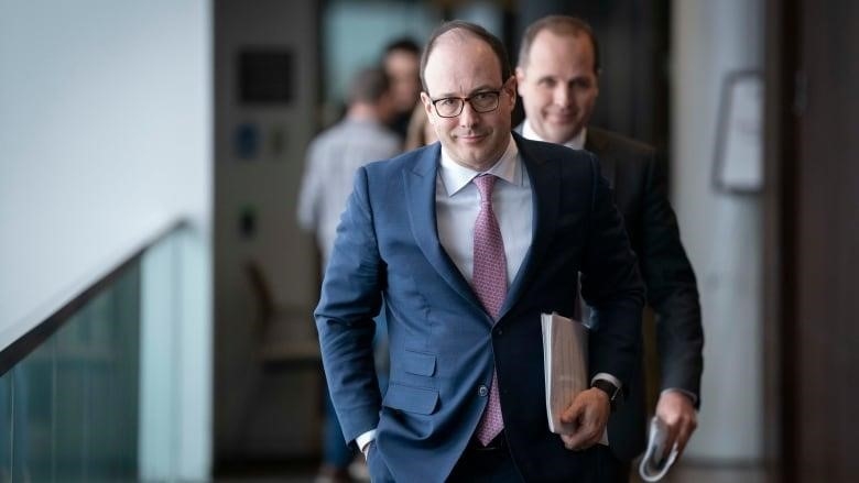 Man in suit walking toward camera, man in background fuzzy