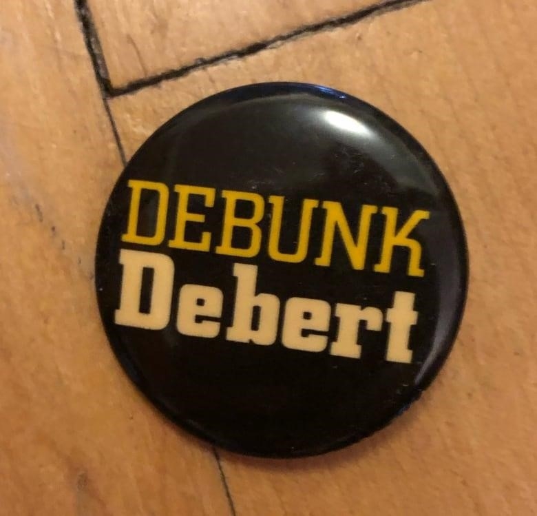 This is a black button. On it is the text Debunk Debert. 