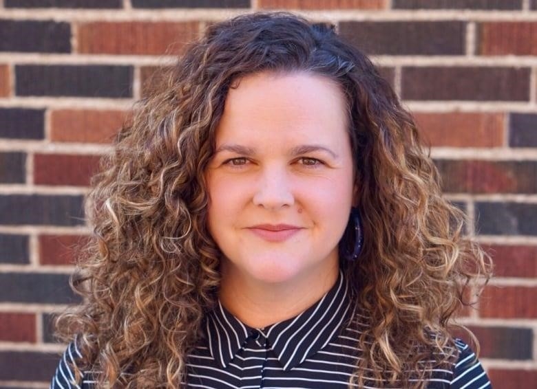 woman with curly hair and blue striped shirt smiling