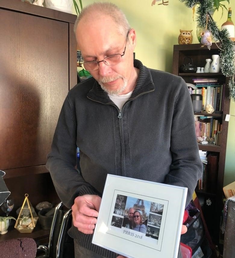 A man with short grey hair holds a framed photo of himself and a woman in Paris.