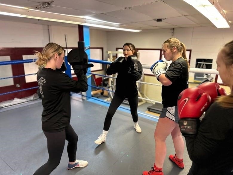 Three young female boxers practice in a ring 