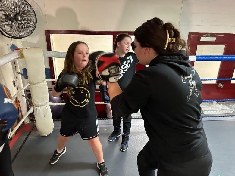A boxing coach instructs three young boxers in the ring 