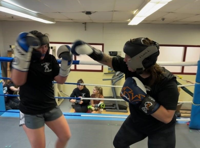 Two female boxers with head protection and gloves are sparring in a ring 