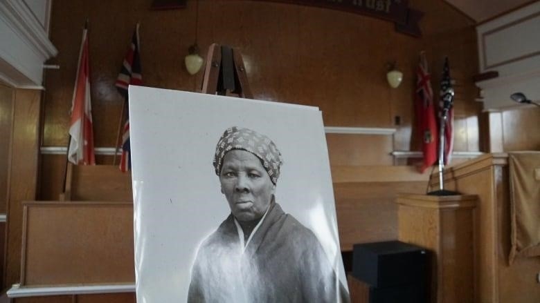 A portrait of older Black woman, Harriet Tubman, sits in the middle of a church. 