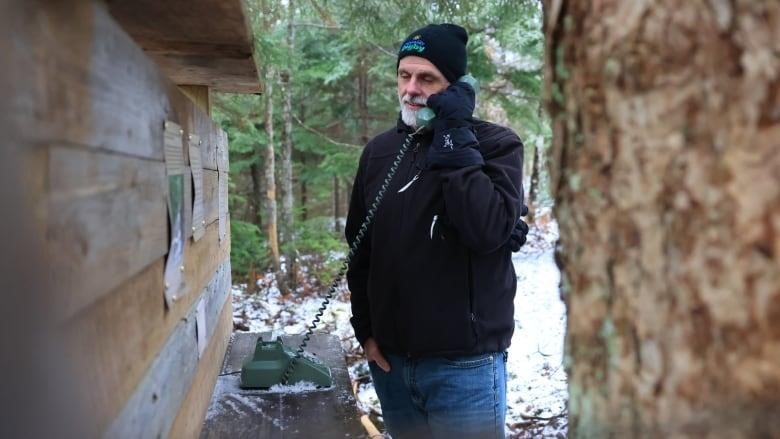 A man holds a rotary phone receiver in his hands in the woods on a snowy day.