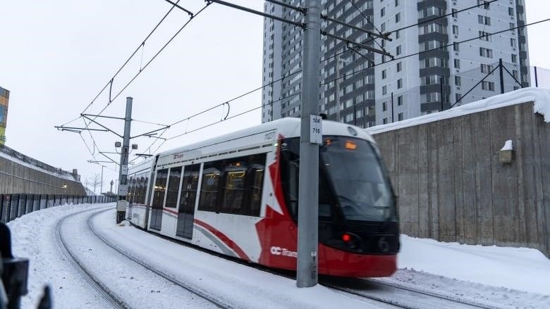 A red-and-white train travels along a track in the snow.