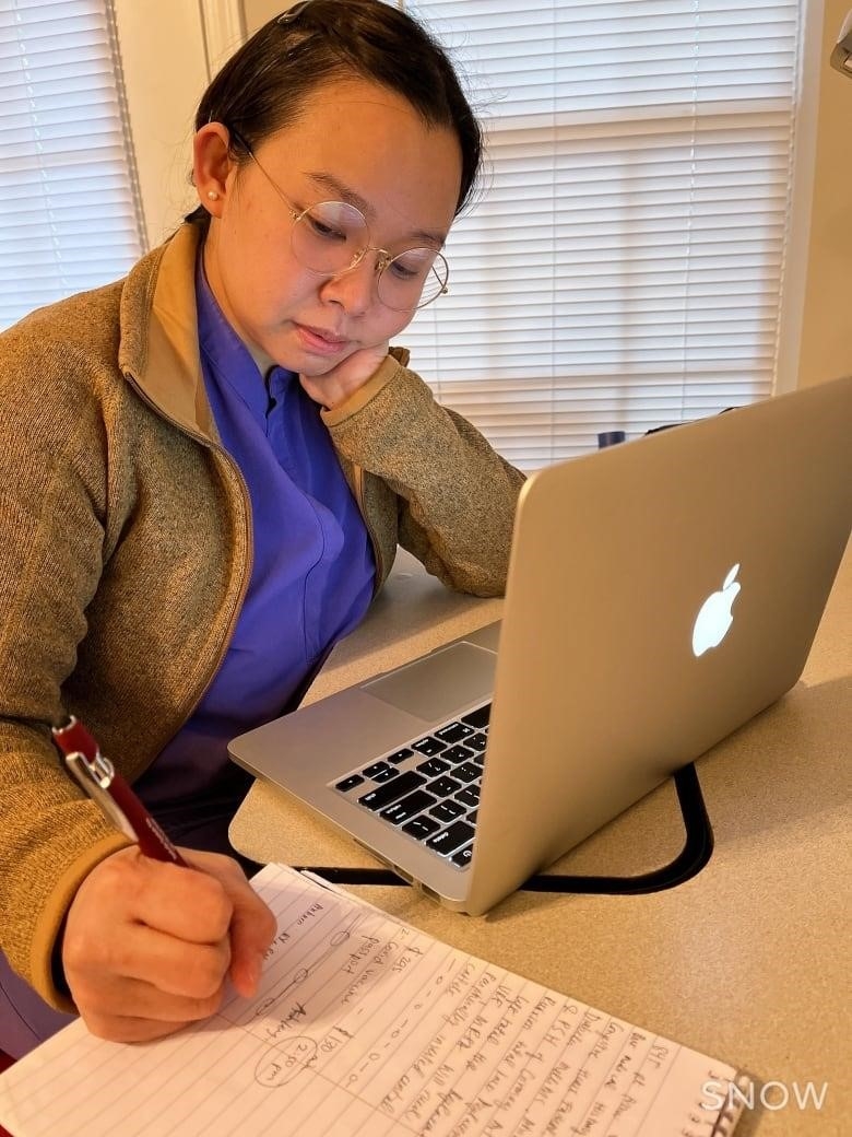 A nurse wearing a mask stands beside a medical monitor.