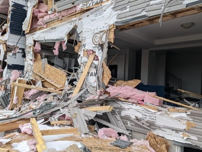 Broken plywood and insulation surrounds the frame of a house. 