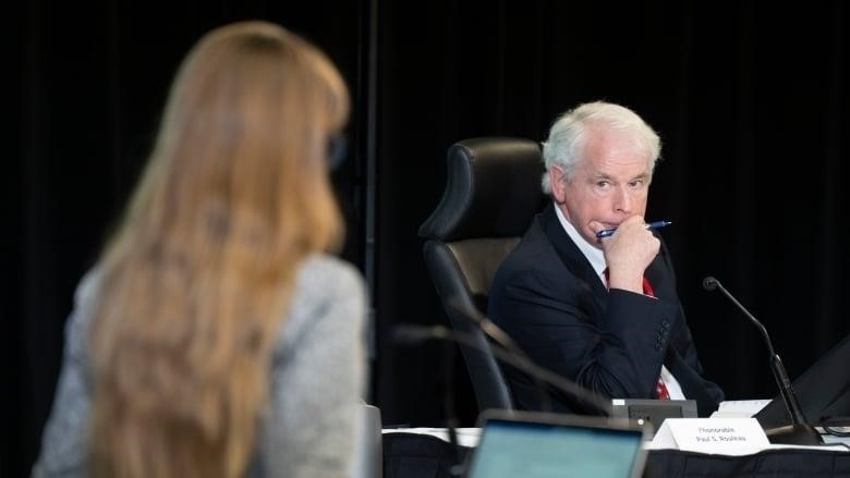 A man in a suit at a desk listens to a speaker.