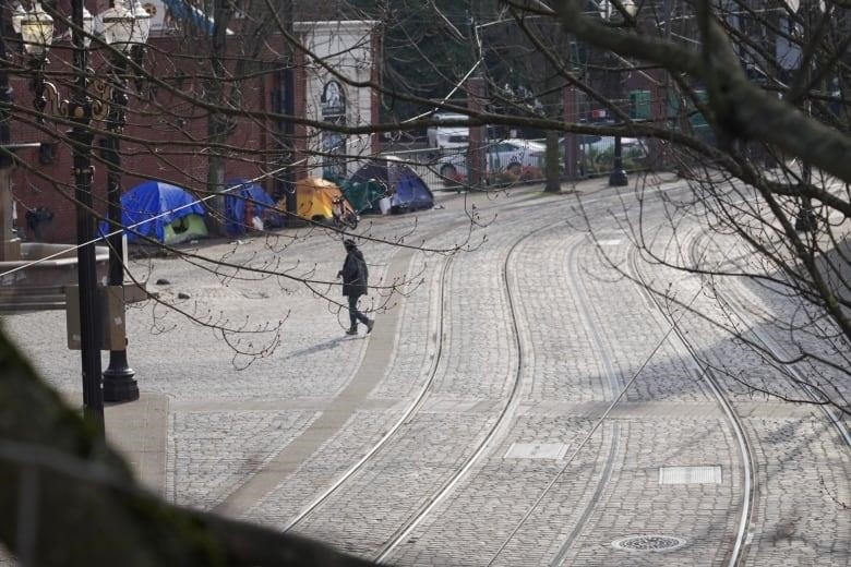 A cobblestone street in Portland with a line of tents along the side of a building where people are living. 