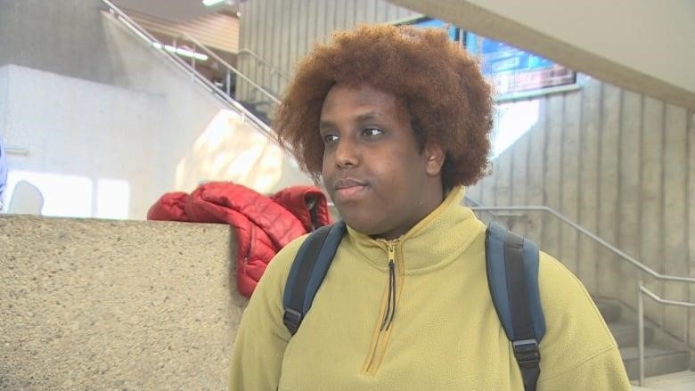 A man with an afro and a yellow jacket stands by a stairwell.