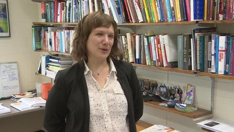 A woman clad in a suit stands next to rows of books.