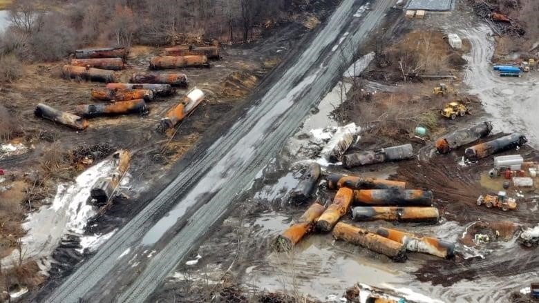 The burnt remnants of freight cars piled up along either side of a railway track.