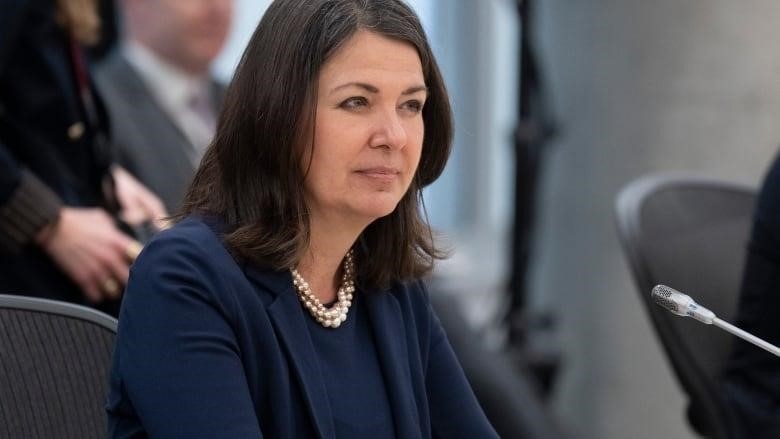 Alberta Premier Danielle Smith sits at a table with a microphone near here, as she waits for a meeting on health-care with the prime minister to begin, Tuesday, February 7, 2023 in Ottawa. 