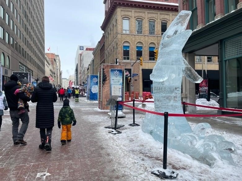 People walk on a city pedestrian street in winter next to a ice sculpture of a large fish.