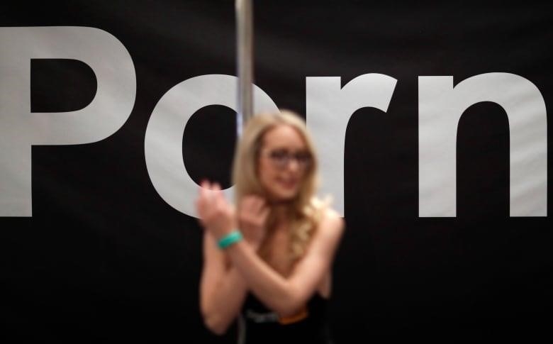 A woman stands in front of a pole and a large sign that says "Porn."