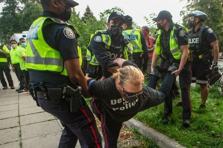 An encampment supporter is detained by the police as city officials work to clear the Alexandra Park encampment in Toronto.