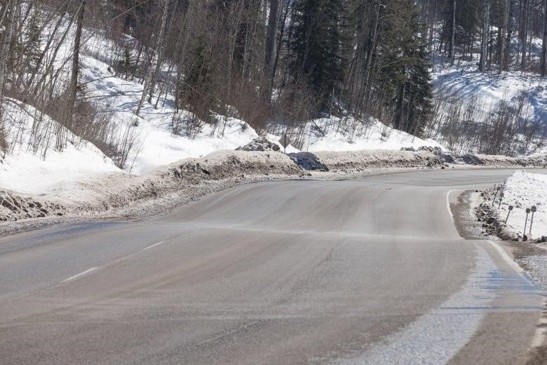 A lumpy stretch of highway is seen cutting through a snowy forest.