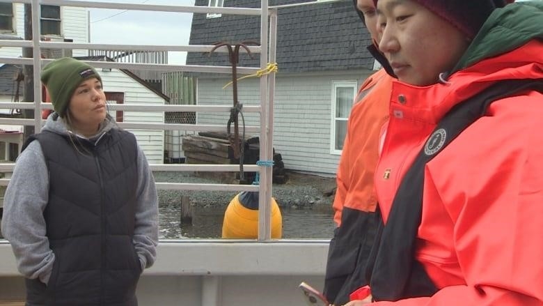 A woman is shown on a fishing boat talking to two men in bright red jackets.