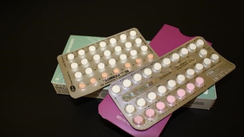 A package of birth control pills is seen on a black surface.