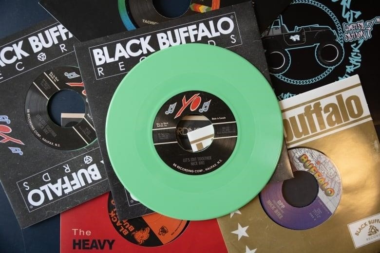 Several records are shown overlapping each other on a table with a green single in the middle.