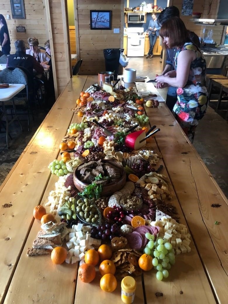 A charcuterie board filled with meats, cheeses, fruits and other finger foods is laid out on a long wood table at a wedding reception.