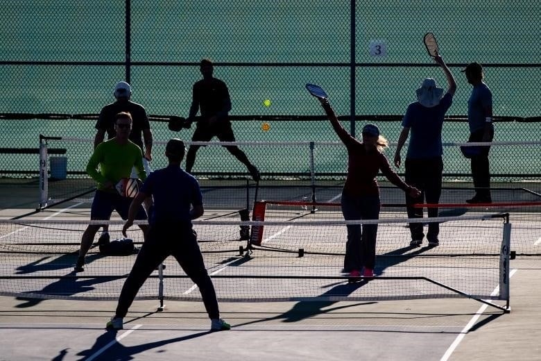 People in silhouette play pickleball.