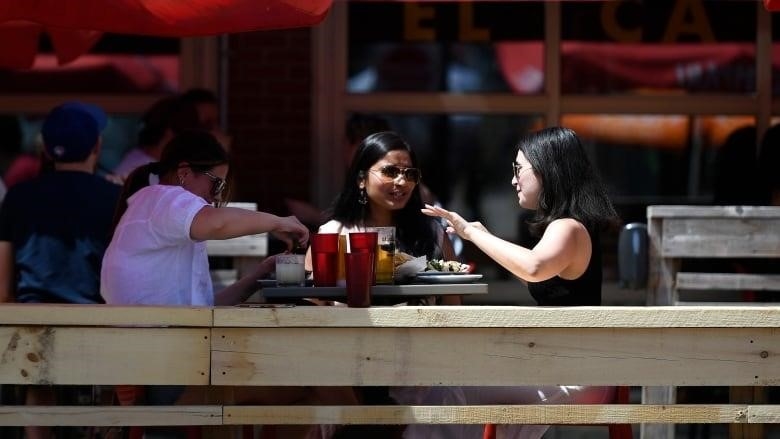 Two women wearing sunglasses sit on a patio. 