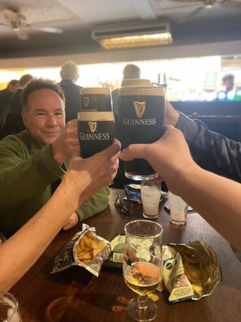 A man and three other arms reach out to cheers with their pints of Guinness