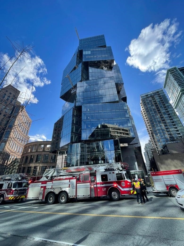 Fire trucks surround an irregularly shaped skyscraper with a window-cleaning boom jutting out halfway up.