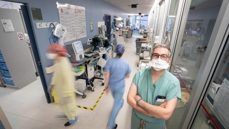 A man stands in a bustling hospital intensive care unit. 