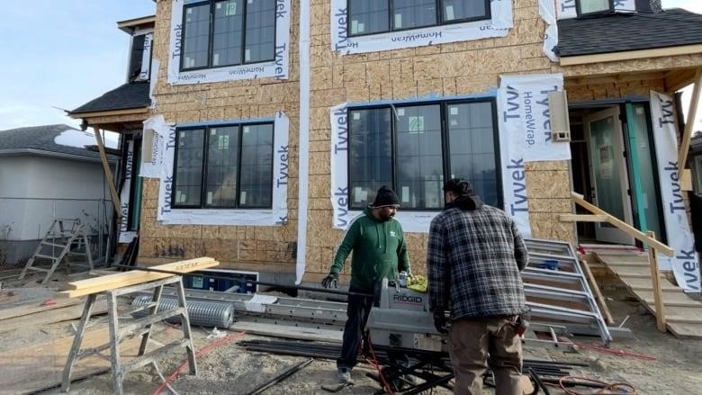 Two workers stand in front of a two-storey duplex under construction in the southwest community of Shaganappi.