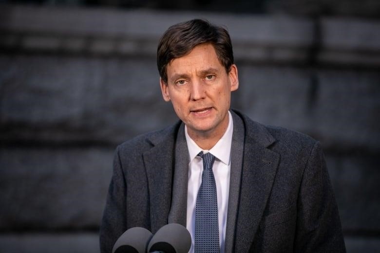 A white man wearing a suit speaks at a podium. He is clean shaven.