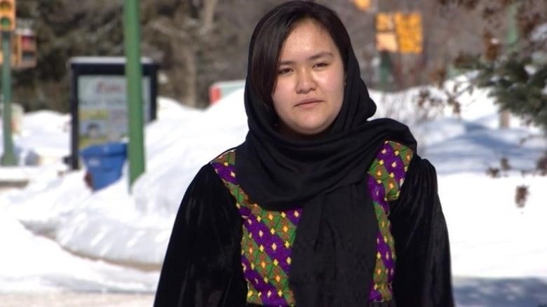 A girl in a black head scarf walks down the street.