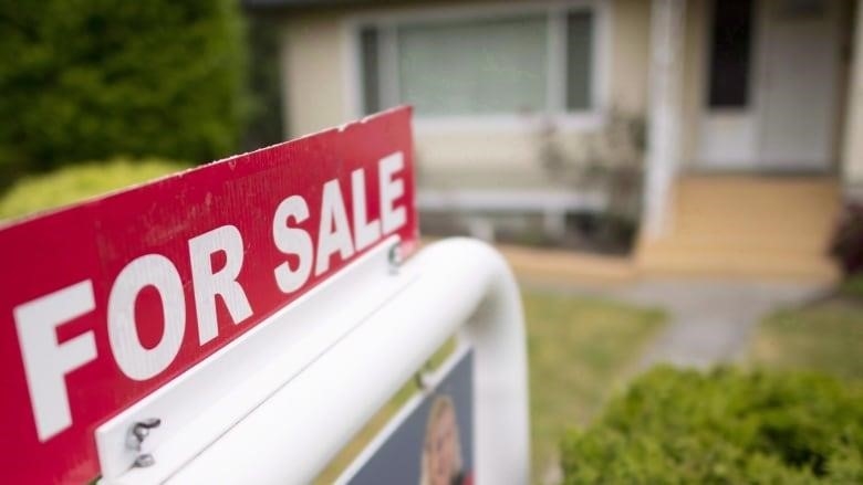 A real estate sign in front of a house that reads 'FOR SALE'.