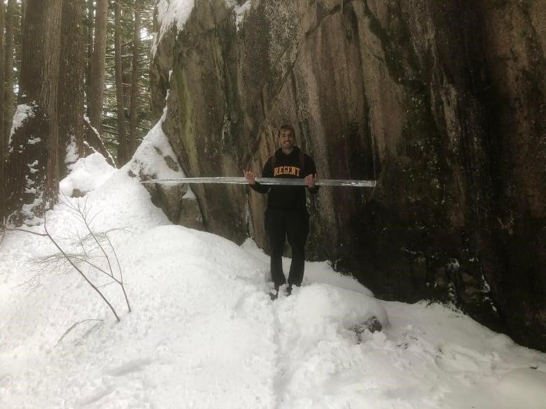 Benjamin Munnalall holds the icicle lengthwise in his hands in front of a rock face which he have snapped off in the Stawamus Chief Trail in Squamish. 