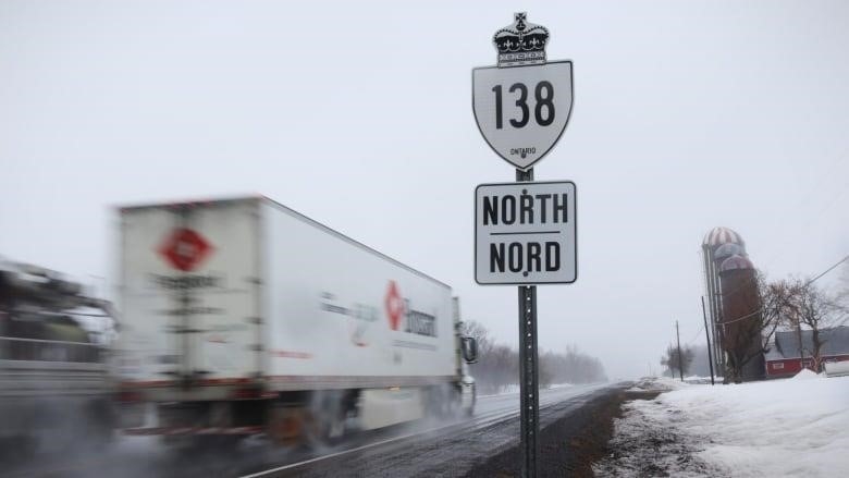 Two trucks travel in opposite directions on a highway in winter.