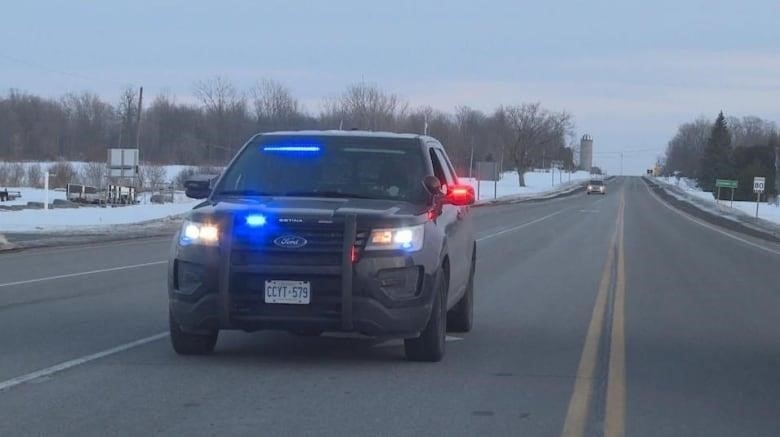 A black police vehicle with its lights on is parked on a highway in winter.
