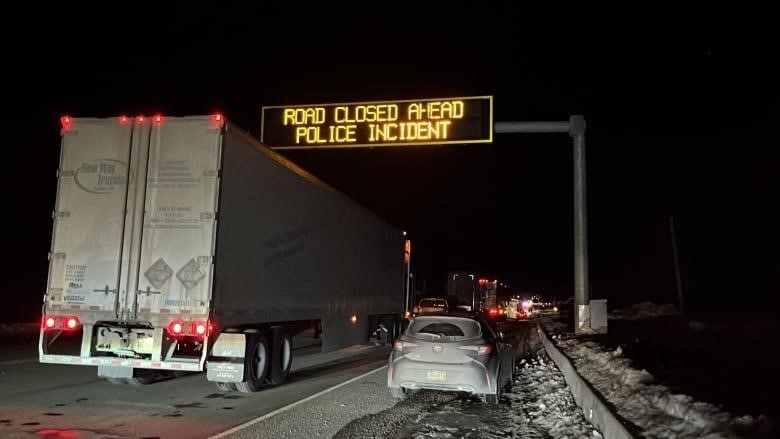 A sign saying 'road closed ahead, police incident' is pictured at nighttime, on a highway filled with traffic.