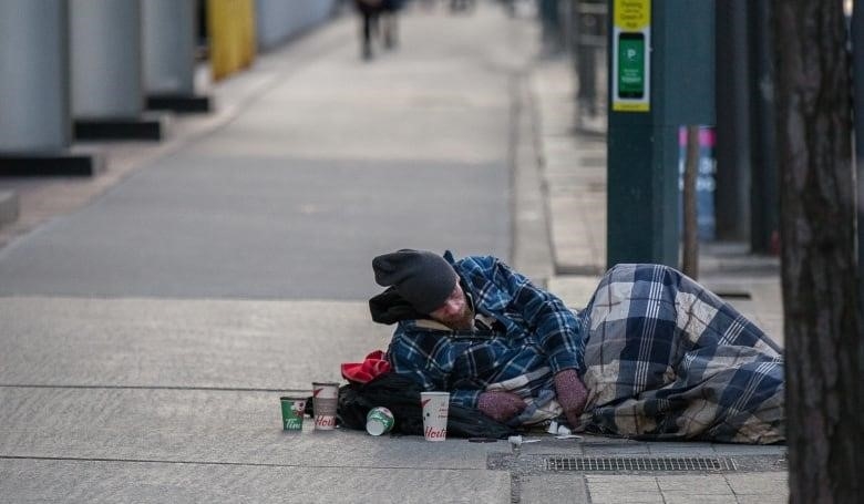 A man under a blanket on a sidewalk in Toronto. 