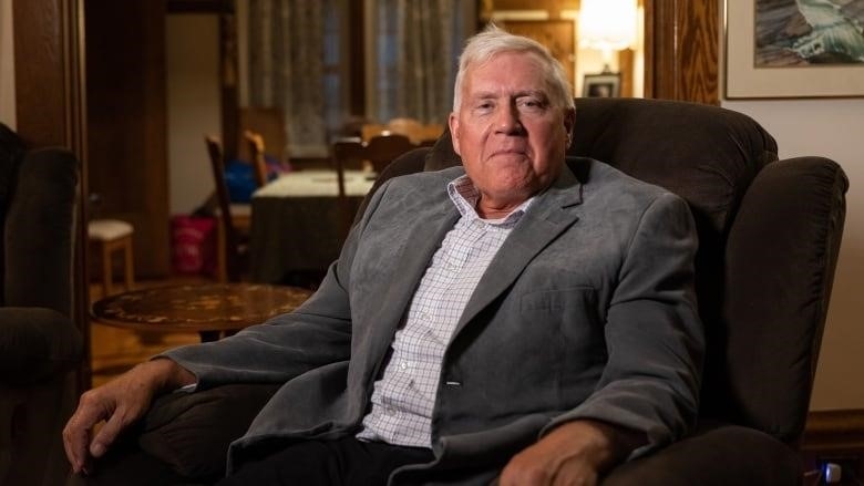 A man wearing a sports jacket sits in an armchair.