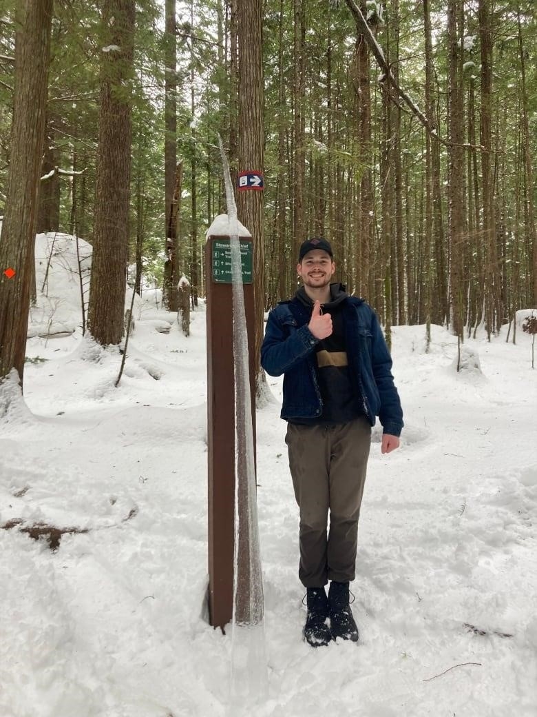 Mitchell Vander Ploeg stands in front of the icicle standing upright against a sign post in the Stawamus Chief Trail in Squamish. 