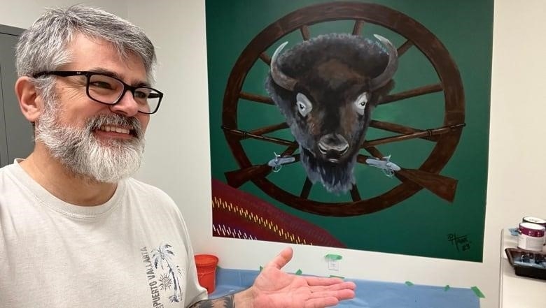 A man stands in front of a mural painting depicting a bison head.