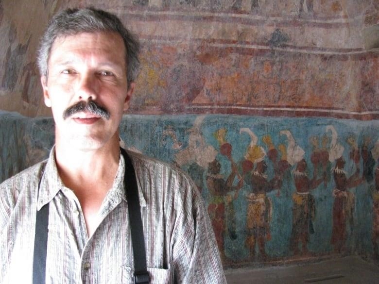 A man stands in front of cave paintings. 