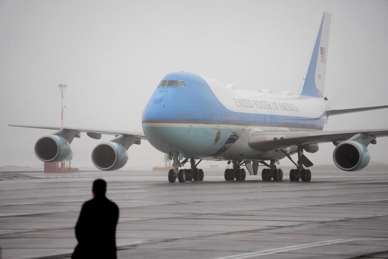 A large blue and white plane on a runway in fog.