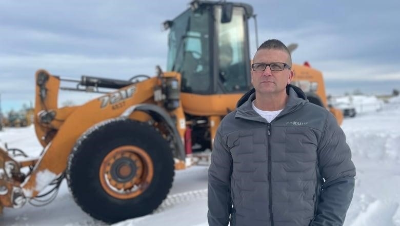 A man stands in front of a snow plow.