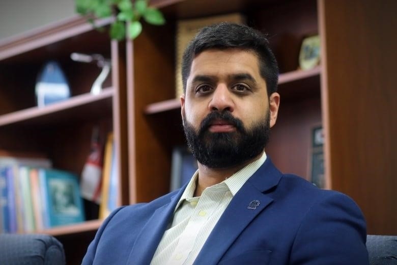 A man in a suit poses for a photo in front of a bookshelf.