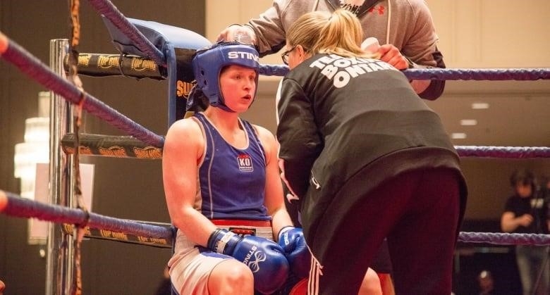 Kaitlyn Clark, 30, is former national boxing champion. She stands in front of a boxing ring with her arms crossed.